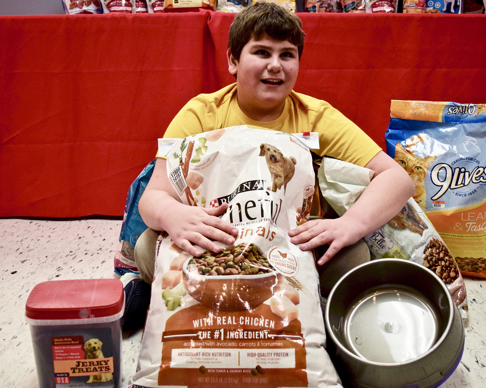 Child sitting with bags of dog and cat food to donate.