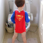 LIttle boy in Superman cape at toilet.